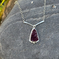 Silver necklace with a druzy amethyst  pendant on a stone surface.