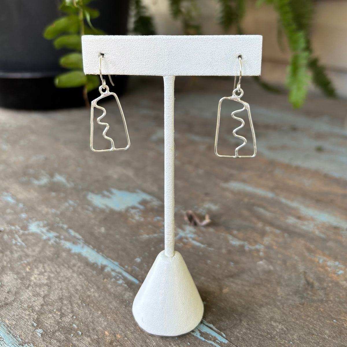 Pair of silver earrings on a white stand with a blurred background