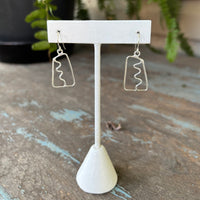 Pair of silver earrings on a white stand with a blurred background