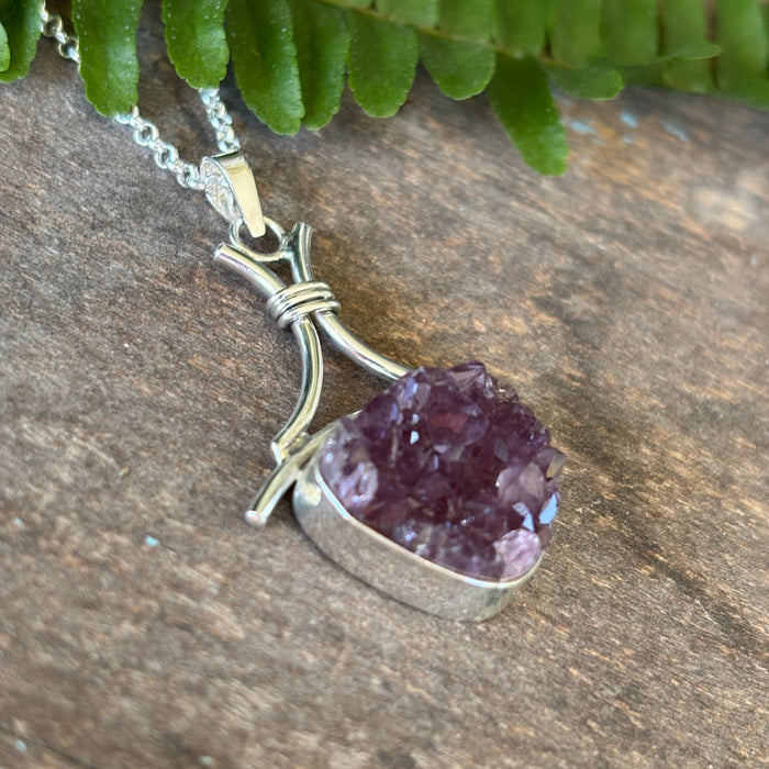 Druzy Amethyst pendant on a silver chain with a green leaf on a wooden surface