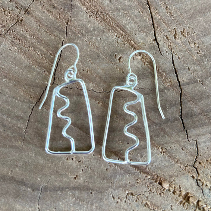 Pair of open work silver earrings with a squiggle down the center on a wooden surface 