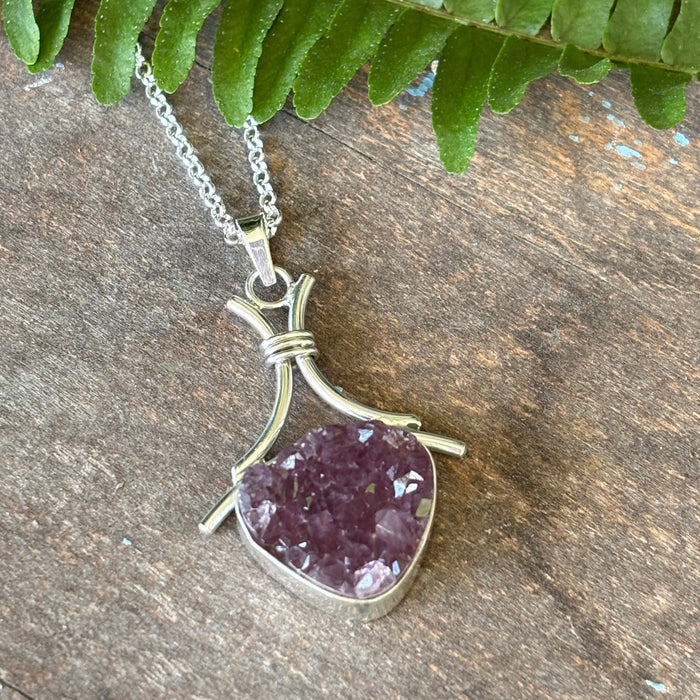 Druzy Amethyst pendant on a silver chain with a green leaf on a wooden surface