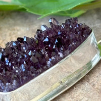 Close up of Amethyst crystal cluster in a silver setting with a green leaf background