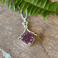 Druzy Amethyst pendant on a silver chain with a green leaf on a wooden surface