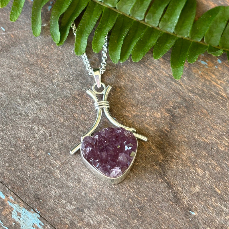 Druzy Amethyst pendant on a silver chain with a green leaf on a wooden surface