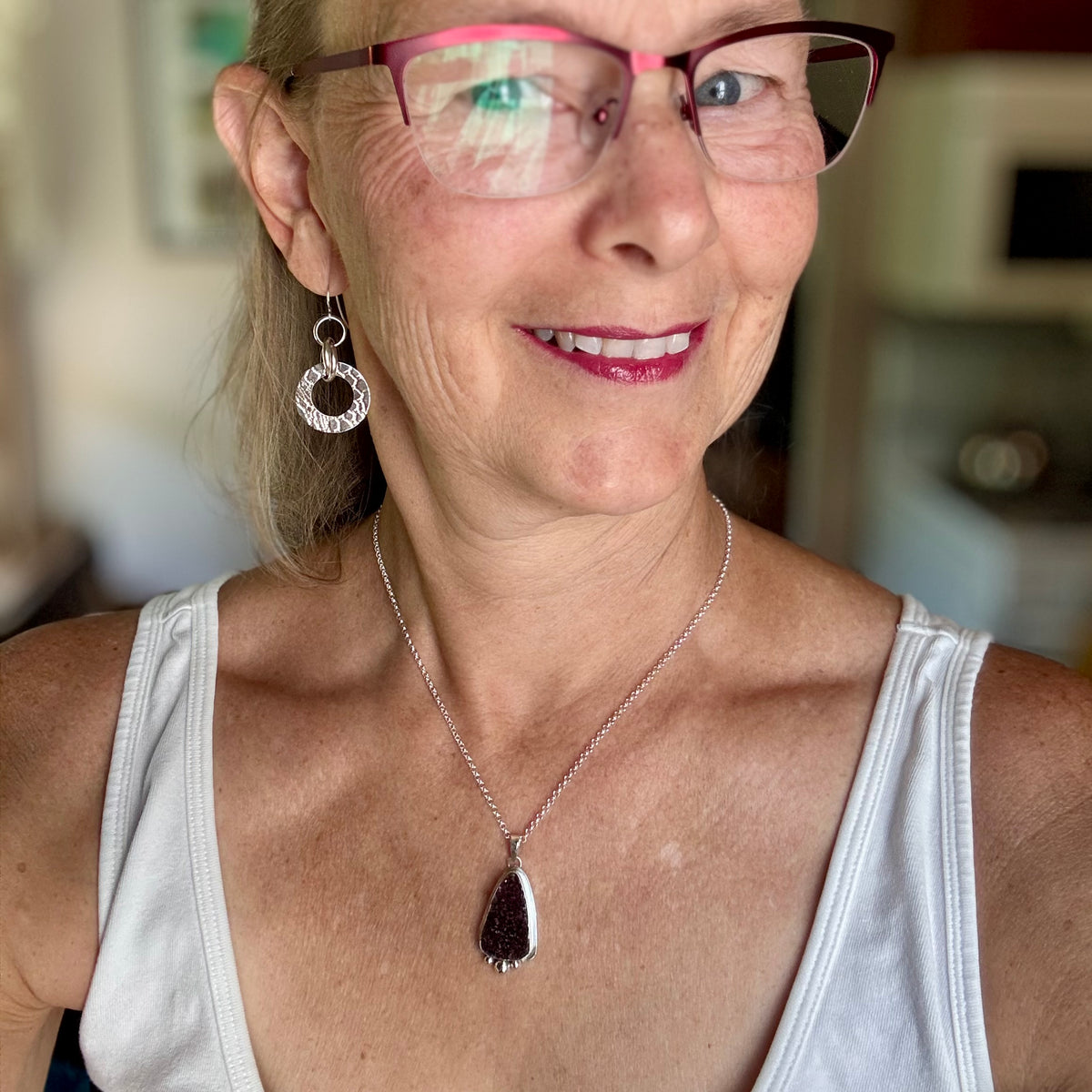 Woman in a white tank wearing glasses and a druzy amethyst necklace. that she created herself.