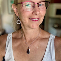 Woman in a white tank wearing glasses and a druzy amethyst necklace. that she created herself.