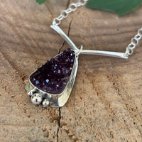 Druzy Amethyst necklace on a wooden surface with a fern leaf