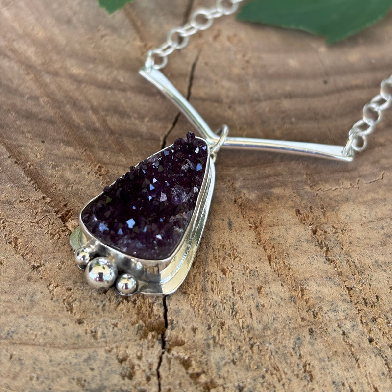 Druzy Amethyst necklace on a wooden surface with a fern leaf