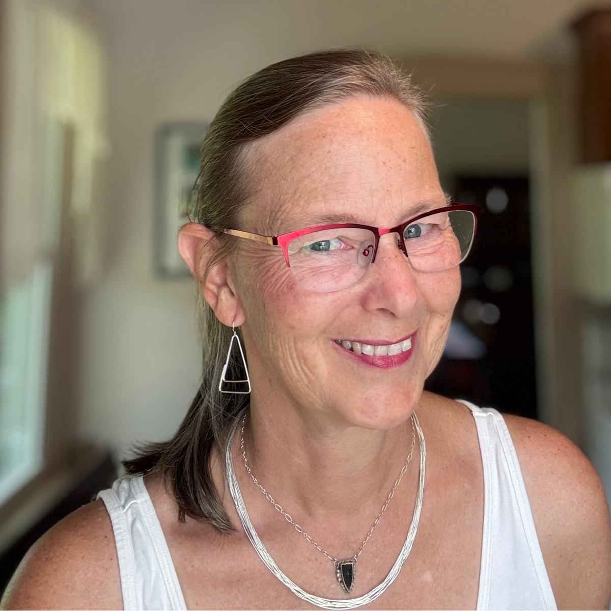 woman with glasses wearing triangular dangle earrings and black druzy necklace