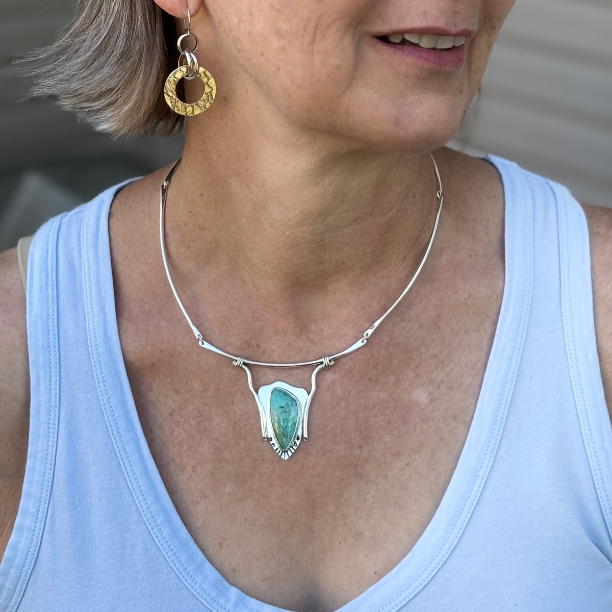 Woman wearing a silver neck collar with a turquoise pendant