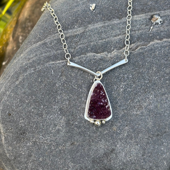 Silver necklace with a druzy amethyst  pendant on a stone surface.