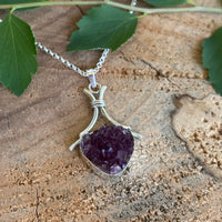 Druzy Amethyst pendant on a silver chain with a green leaf on a wooden surface