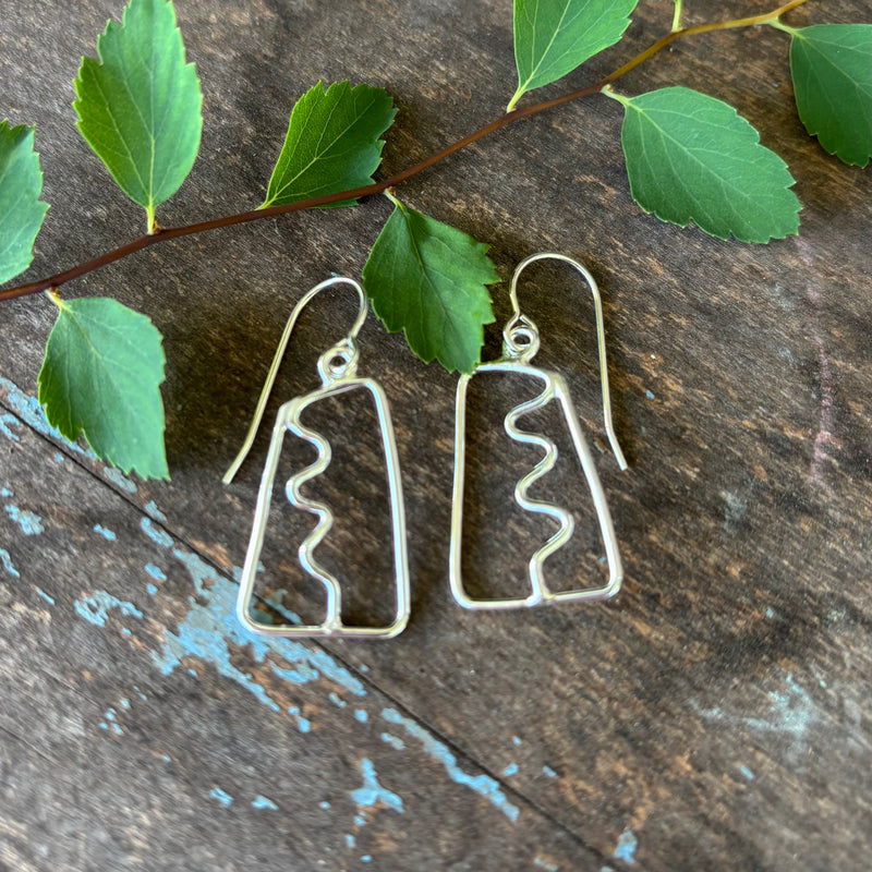 Abstract Silver earrings  with a squiggle down the center on a wooden surface with green leaves