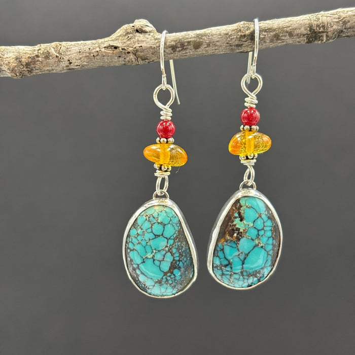 Turquoise earrings with colorful beads on a branch against a dark background