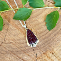 Necklace with a purple pendant on a wooden surface with green leaves.