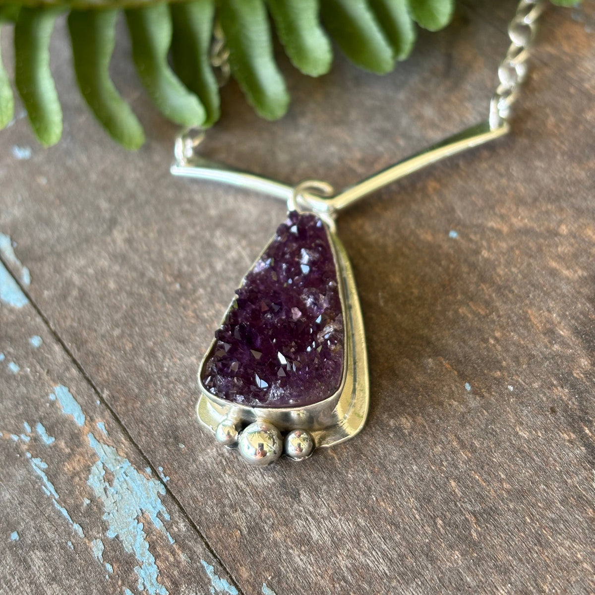 Druzy Amethyst necklace on a wooden surface with a fern leaf