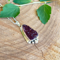 Amethyst druzy pendant on a silver chain with green leaves on a wooden surface