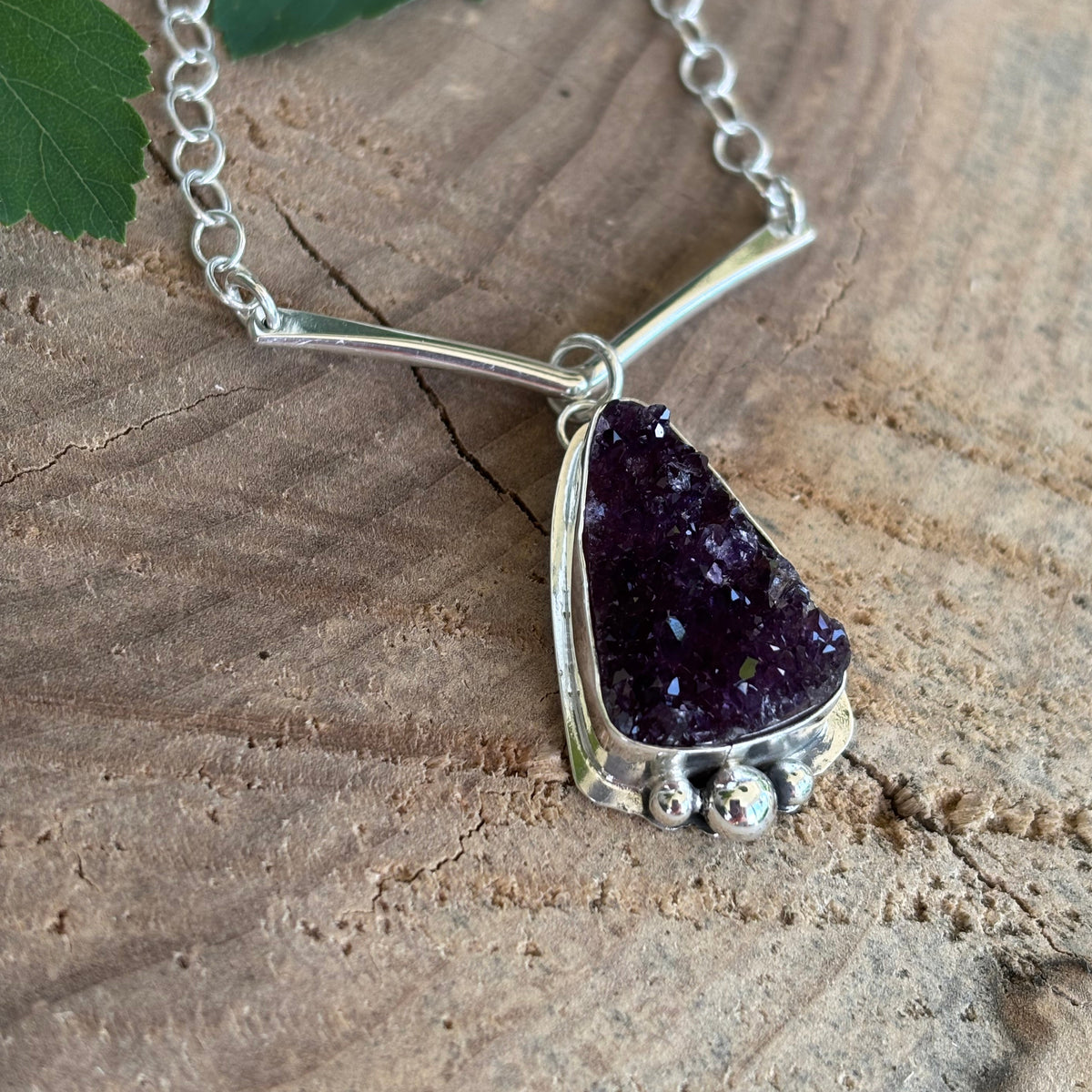 Druzy Amethyst necklace on a wooden surface with a fern leaf
