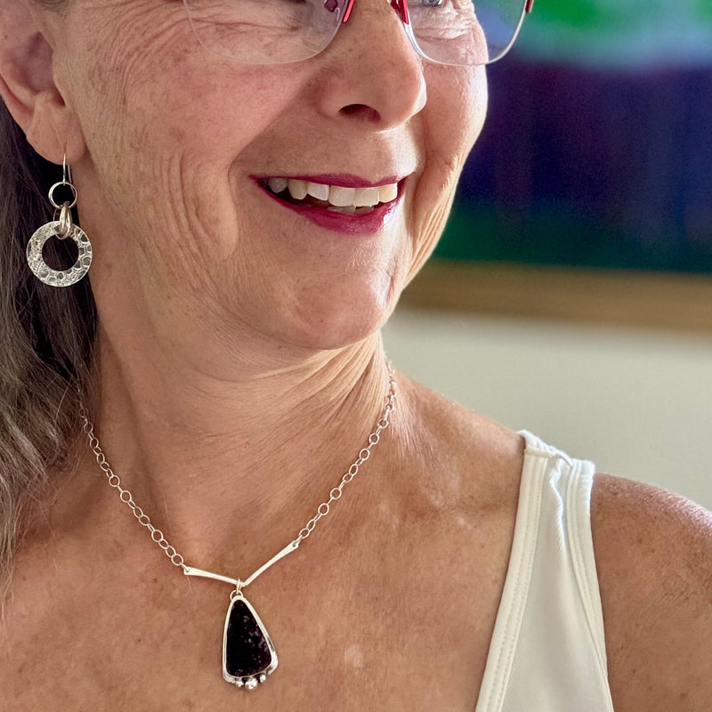 Woman wearing a necklace with a druzy amethyst pendant and earrings, smiling.