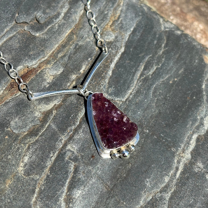 Silver necklace with a druzy amethyst  pendant on a stone surface.