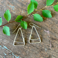 Silver triangle earrings on a wooden surface with green leaves