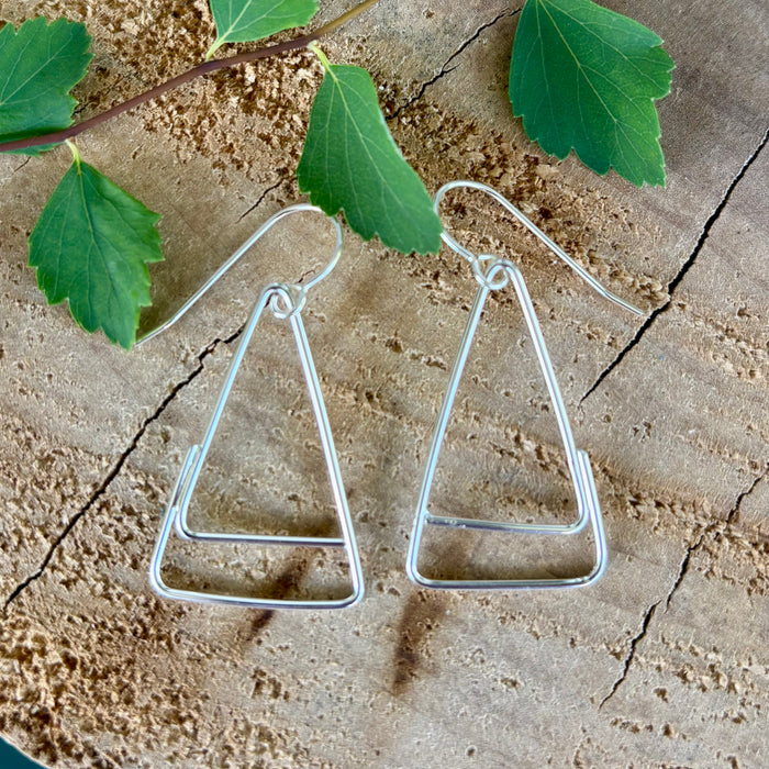 Silver triangle-shaped earrings on a textured surface with green leaves.