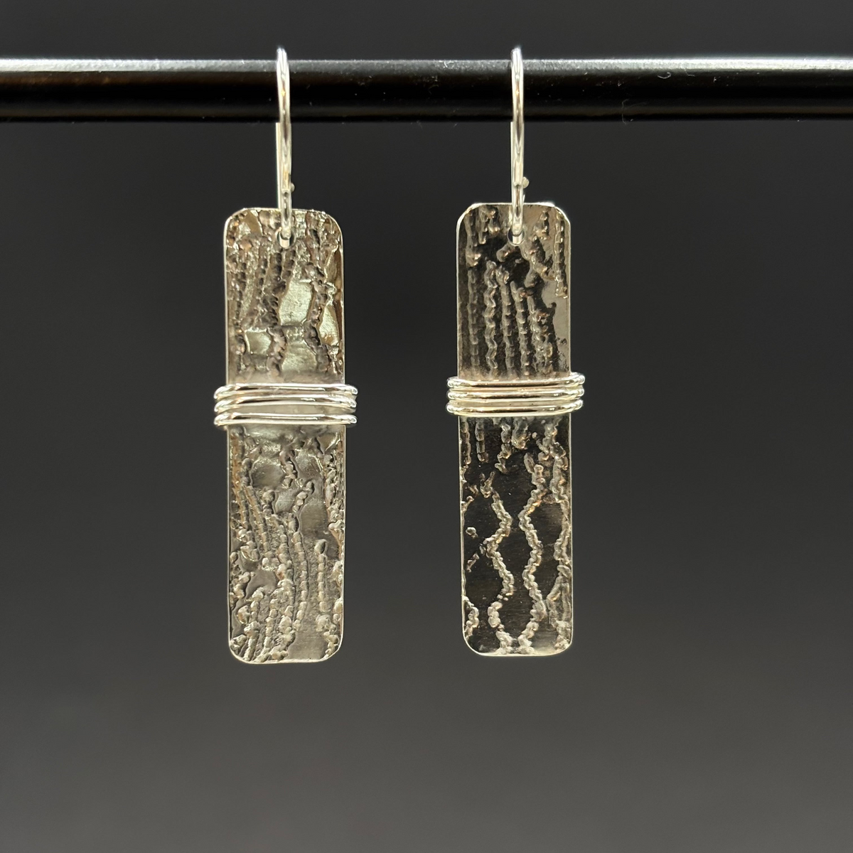 Pair of silver earrings with textured design on a dark background