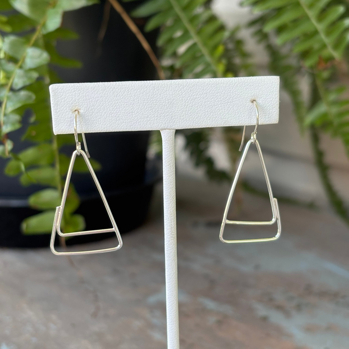 Triangular earrings on a white stand with a plant in the background
